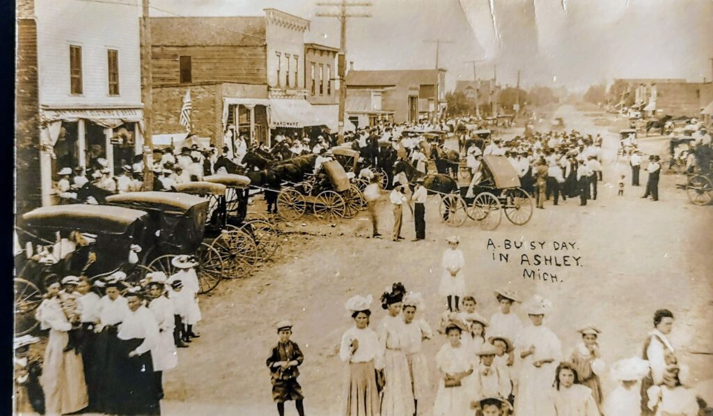 Historic street scene with horse-drawn carriages and crowd.