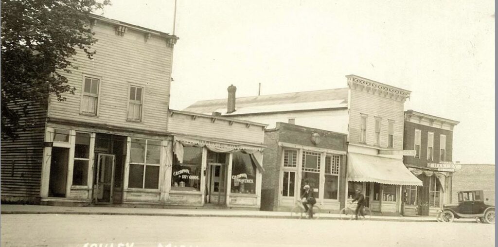 Vintage small-town street with storefronts, bicycles, car.